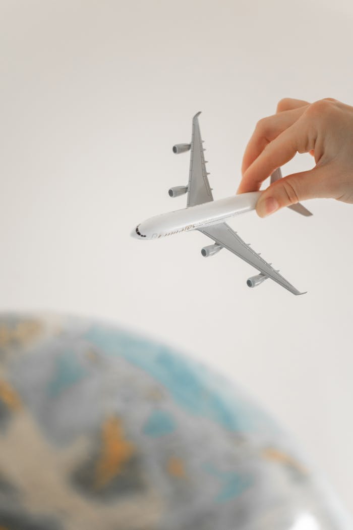 Close-up of a hand holding a toy airplane over a blurred globe, representing travel planning and adventure.